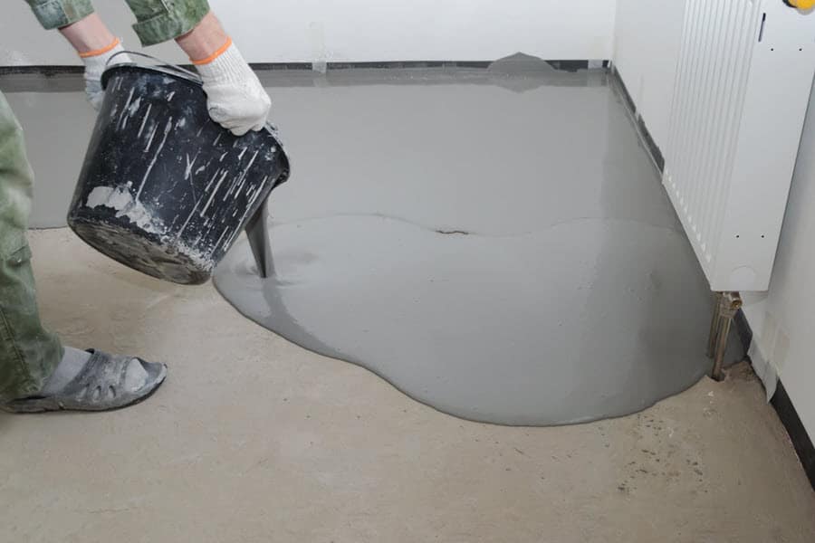 Person applying grey epoxy paint to workshop floor.